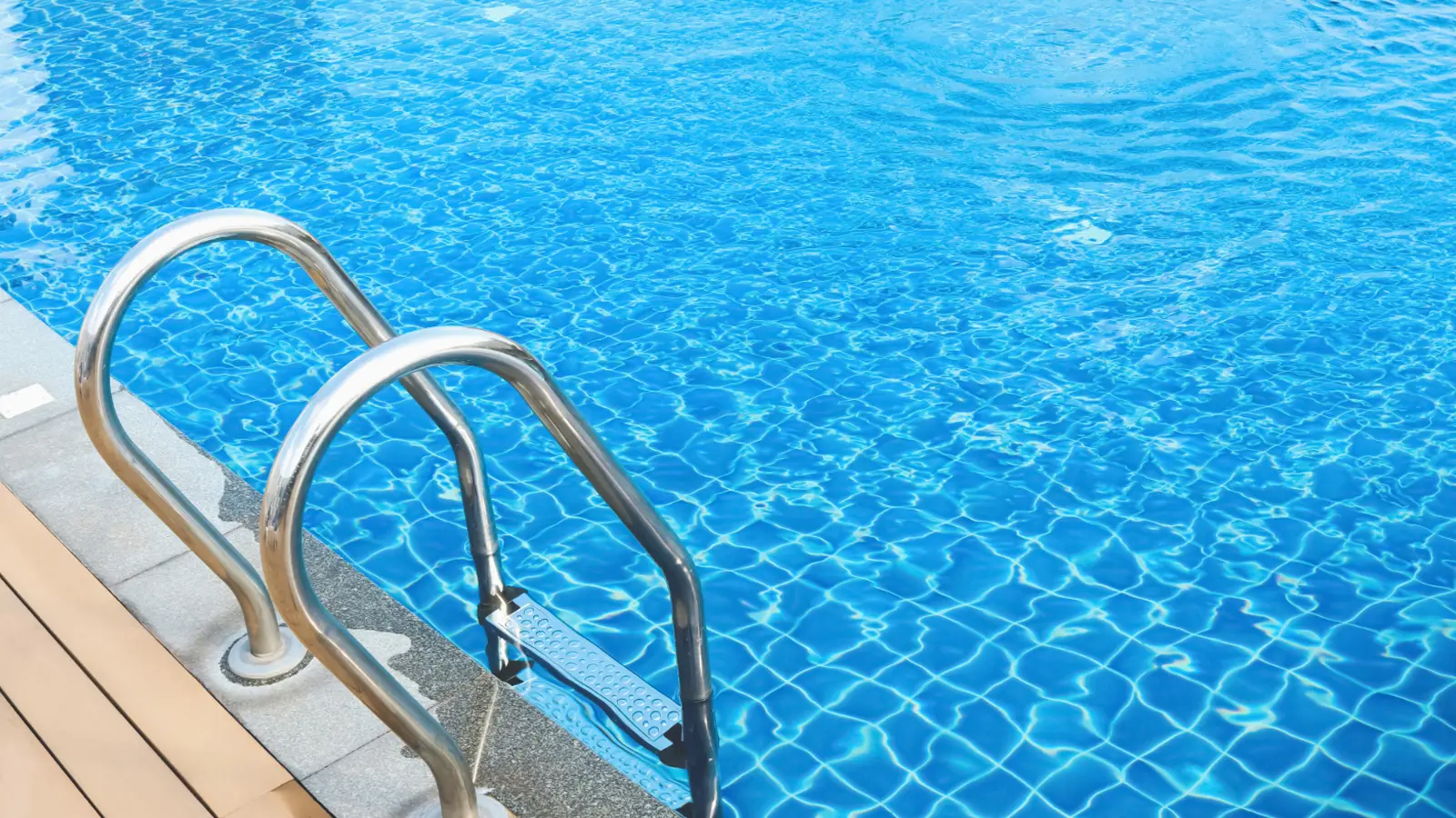 Fotografía que demuestra el mantenimiento profesional de piscina comunitaria en Cunit con escalera de acero inoxidable y acabado de solarium en tarima de madera